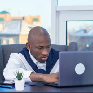 Adult male focused on work at his desk with a laptop in a modern office setting.