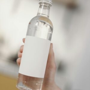 Clear bottle held by a hand with blank label for branding mockup. Minimalist design with a soft focus background.