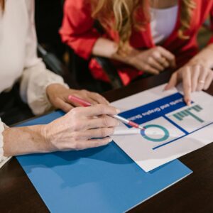 Two women analyzing business charts and reports during a meeting at a wooden table.